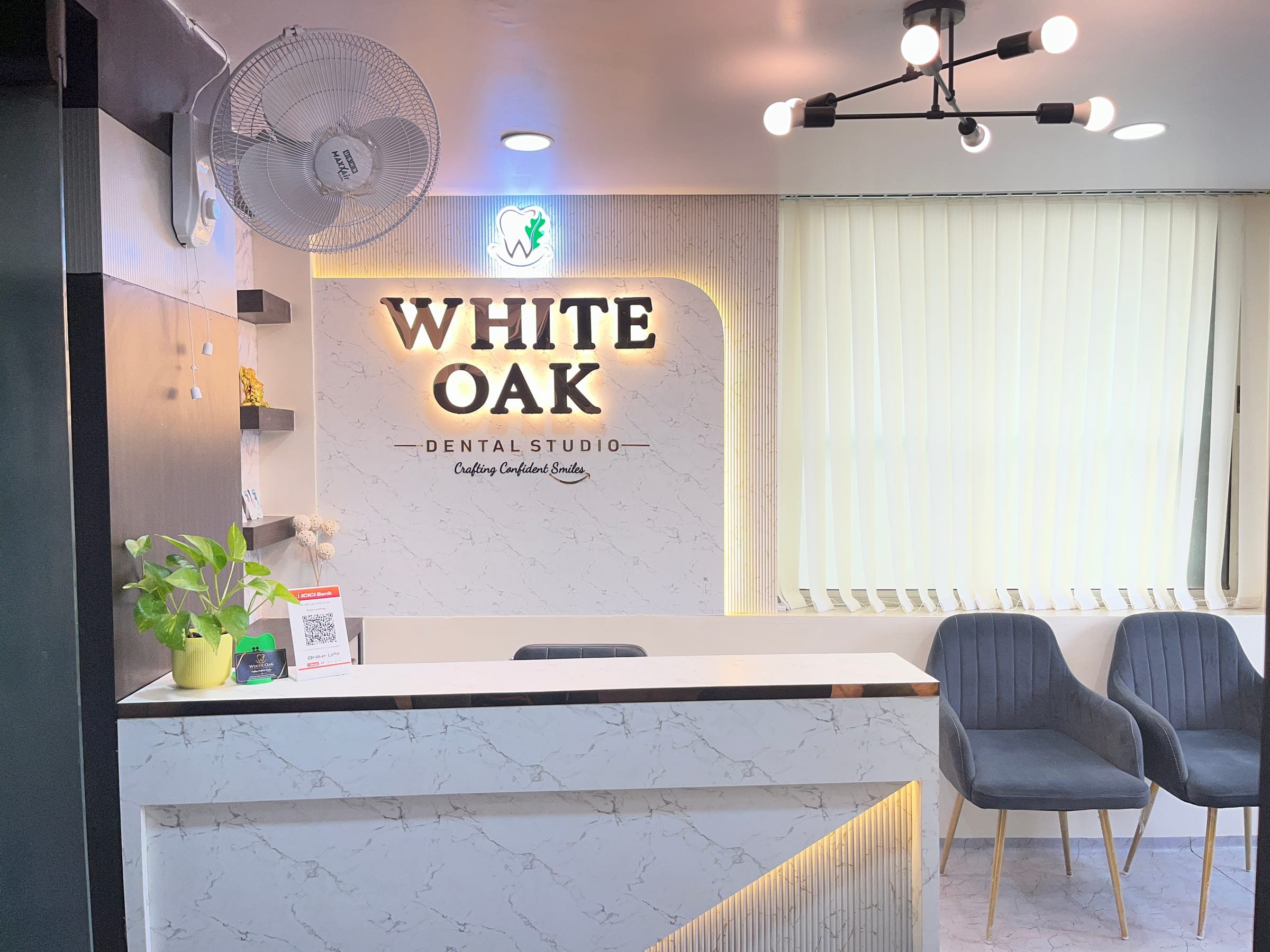Reception desk under the backlit White Oak Dental Studio sign, with lounge chairs beside it, at the clinic in Morabadi, Ranchi