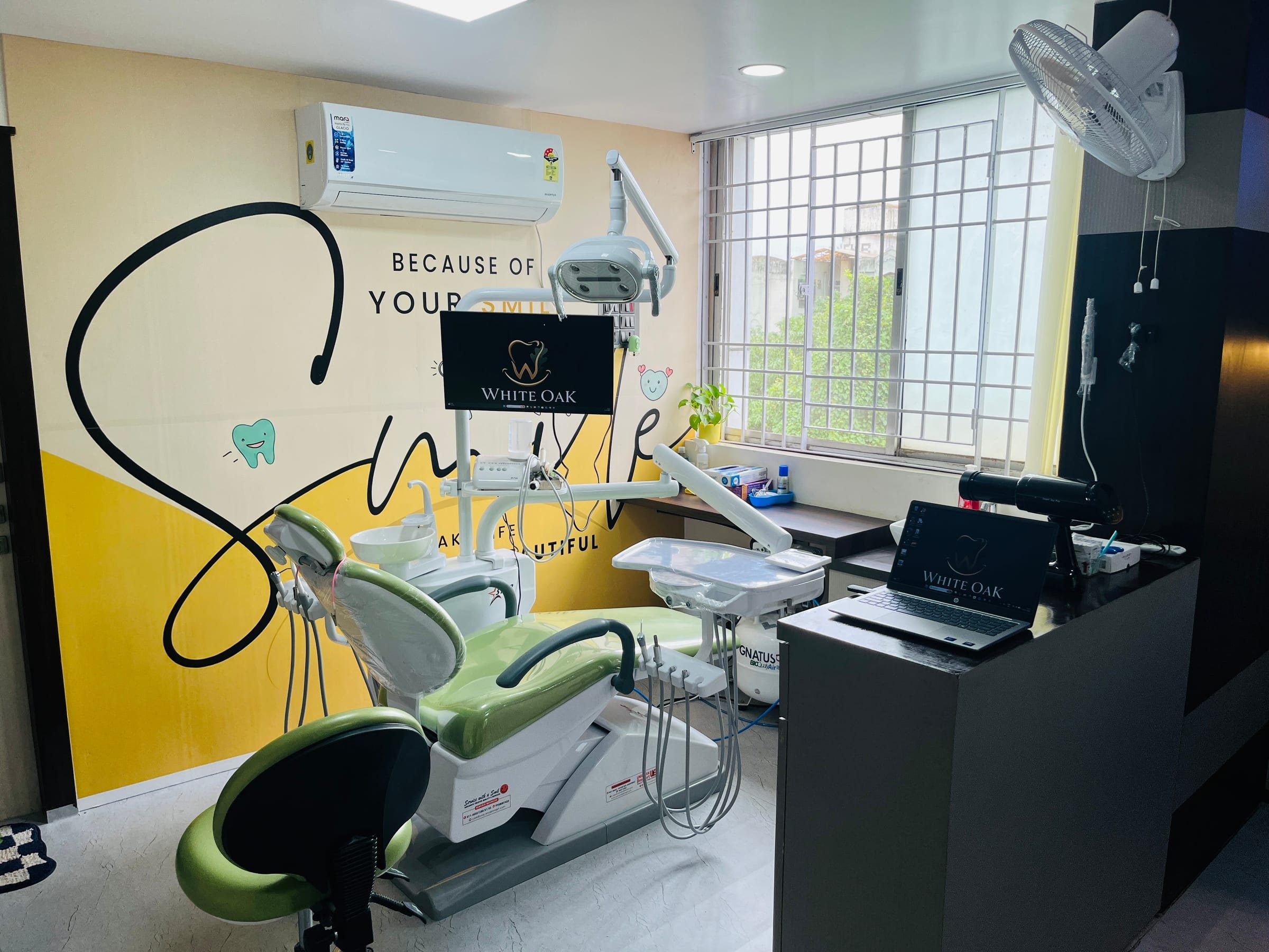 Dental treatment suite with a patient chair, overhead light and a “Because of your smile” mural at White Oak Dental Studio, Ranchi