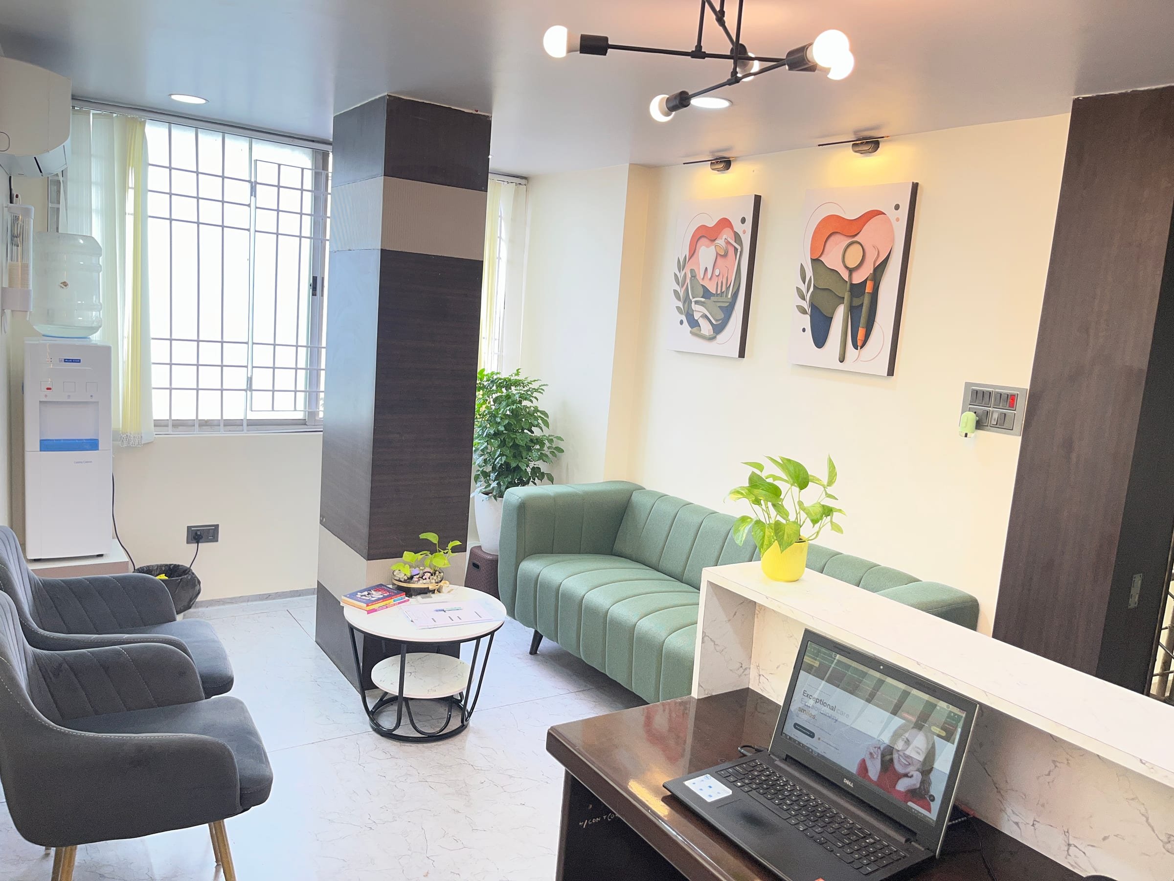 View of the waiting lounge from the front desk, with seating, a water dispenser and framed dental artwork, White Oak Dental Studio